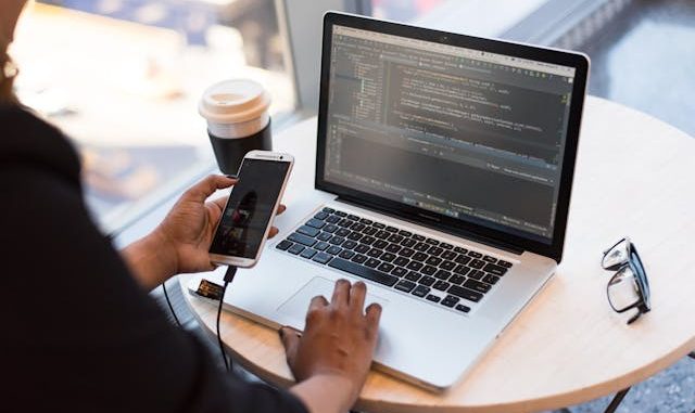 Computer screen with code and mobile on desk.